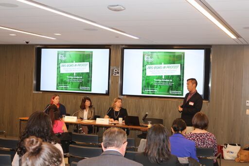 Photo: Introduction of panel participants; 3 panelists seating and moderator standing